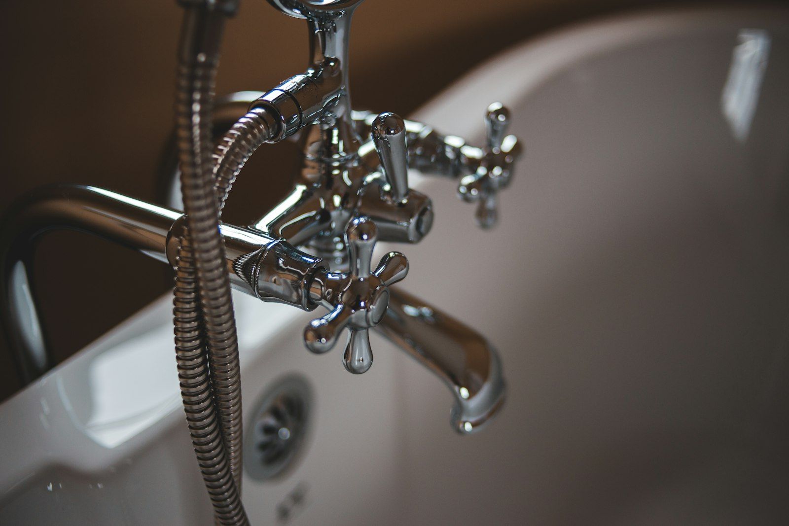 Chrome bath taps and handheld shower on a white bath